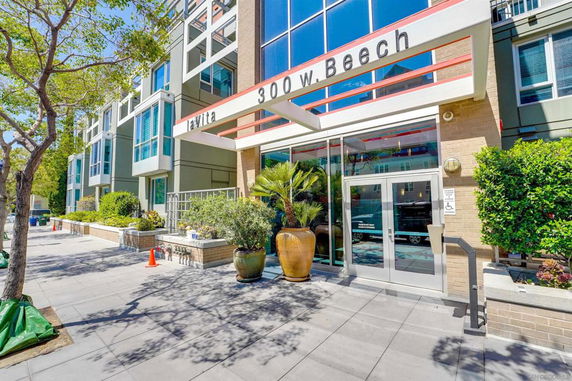 Front view of a modern multi-story building with glass entrance and outdoor planters.