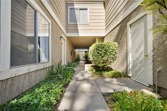 Entrance view of a residential building with a pathway surrounded by small shrubs and plants.