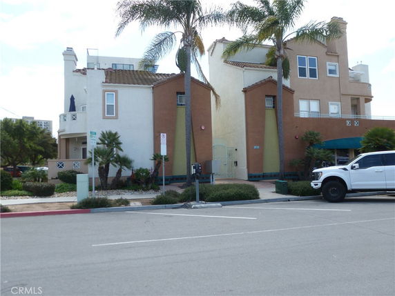 Front view of a multi-story building with a parking space and palm trees.