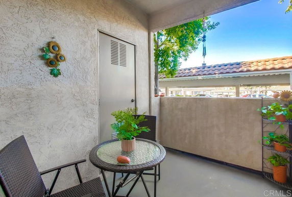 Outdoor patio area with chairs and a table, overlooking a parking area with a tiled roof.