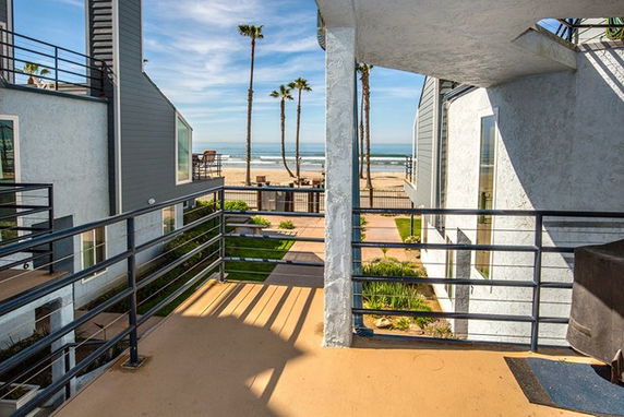 View from a building balcony showing other buildings, palm trees, and the beach with the ocean in the background.