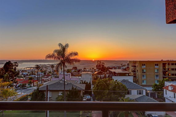Wide angle view of a sunset over a suburban area with buildings, palm trees, and distant water.