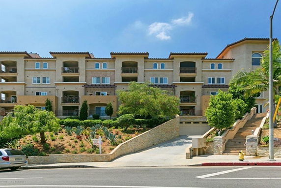 Front view of a multi-story residential building with balconies and a landscaped entrance.