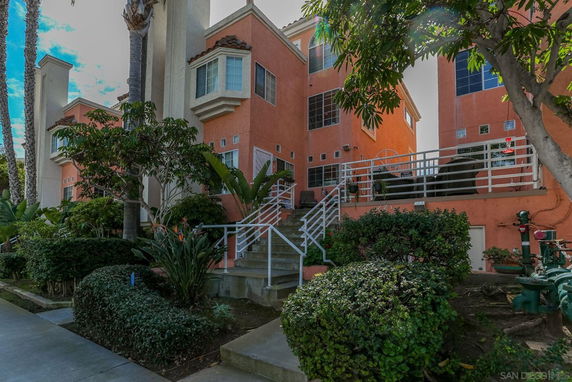 Front view of a multi-story building with white railings and lush green surroundings.