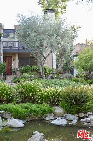 Front view of a multi-story house with a balcony and a garden.