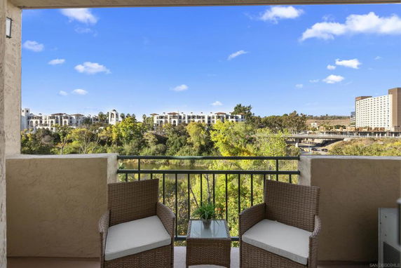 View from a balcony overlooking green trees and a distant urban area.