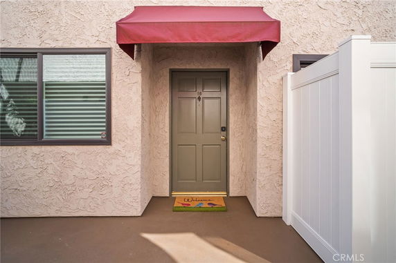 Front entrance of a house with a beige stucco wall, green door, and a red awning.