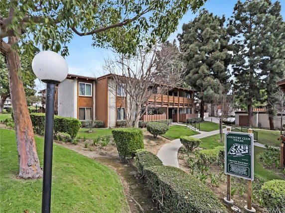 Front view of a two-story apartment building with wooden balconies and a nearby walkway.
