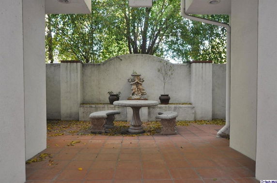 Outdoor patio area with a round stone table, benches, and a decorative statue.