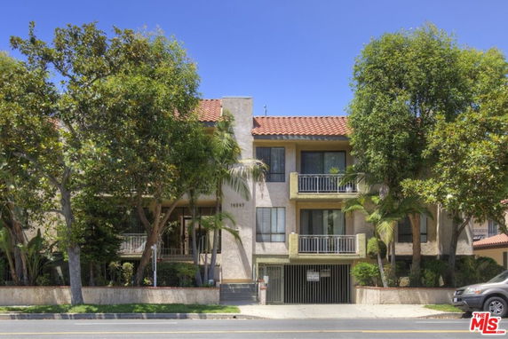 Front view of a multi-story residential building with balconies and a gated entrance at the street level.