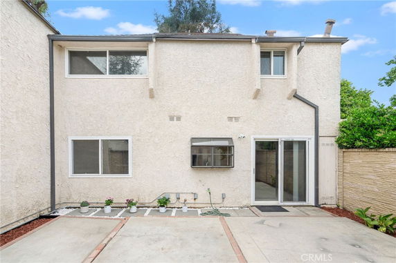 Rear view of a two-story house with beige stucco exterior and sliding glass doors.