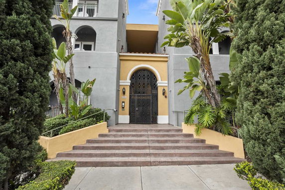 Front view of a multi-story building with an arched entryway and lush landscaping.