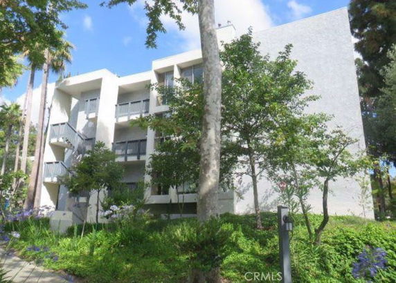 Front view of a multi-story building with balconies surrounded by trees and greenery.