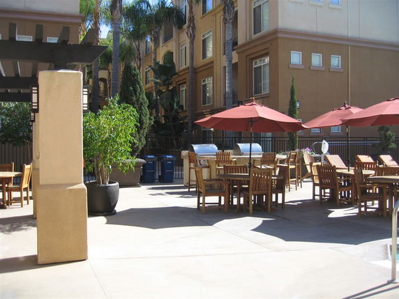 Outdoor seating area with tables, chairs, and umbrellas adjacent to a multi-story building.