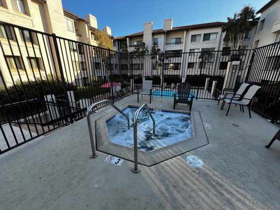 Outdoor area with a small jacuzzi surrounded by a fence and buildings in the background.
