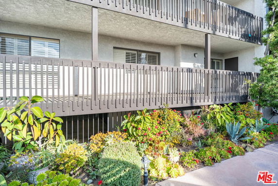 Front view of a building with a two-story balcony and surrounding garden plants.