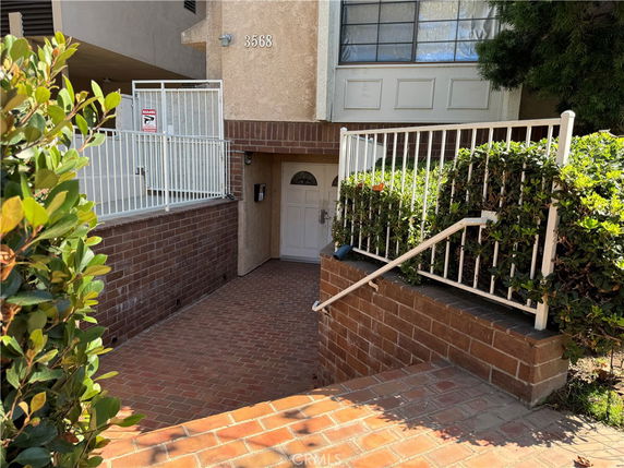 Front view of a building entrance with brick pathway and white railing.