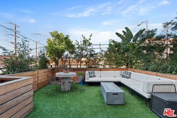 Rooftop seating area with a corner sofa, table, and chairs surrounded by plants.