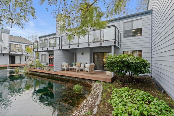 Front view of a modern two-story house with large glass balconies and a wooden deck overlooking a pond.