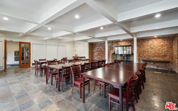 Room with multiple tables and chairs, brick wall, and a television.