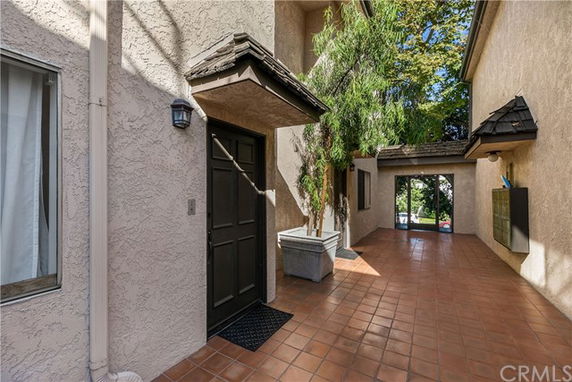 Exterior view of a stucco-finished building entrance with a tiled walkway.