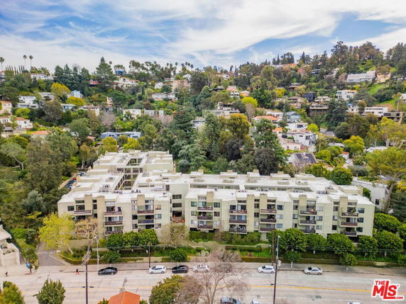 Aerial view of a large apartment complex surrounded by a hilly, wooded residential area.