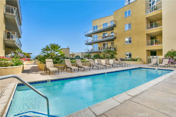 Outdoor swimming pool area with lounge chairs and adjacent multi-story building.