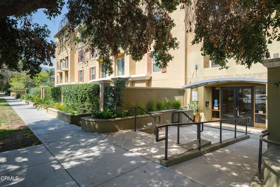Front view of a multi-story residential building with an entrance and surrounding greenery.