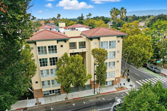 Aerial view of a multi-story apartment building with a red-tiled roof and large windows.