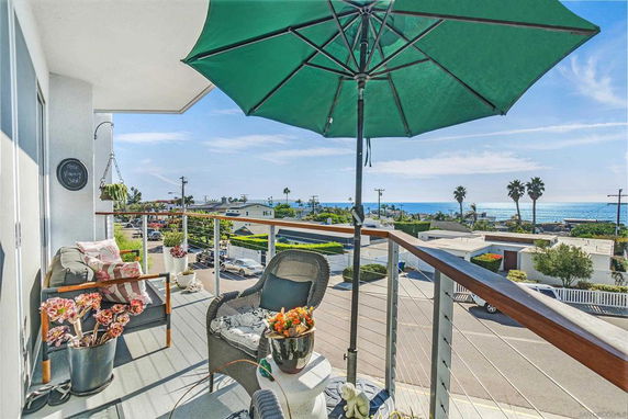 Balcony view with seating area overlooking residential area and ocean.
