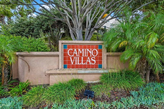 Sign with 'Camino Villas' surrounded by plants and trees.