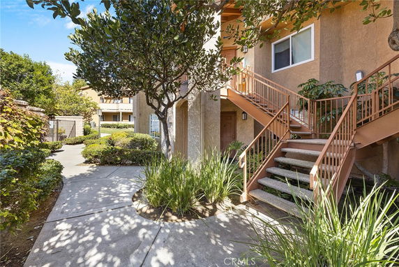 Front view of an apartment building with stairs and greenery.