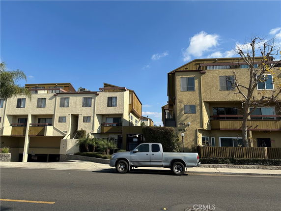 Front view of a multi-story building with balconies and parked vehicles in front.