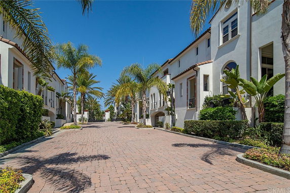 Front view of a row of two-story houses with palm trees lining the path.