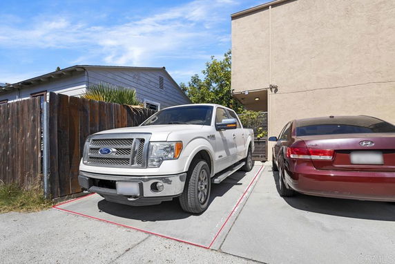Outdoor parking area with a white truck and a red sedan parked beside a building.