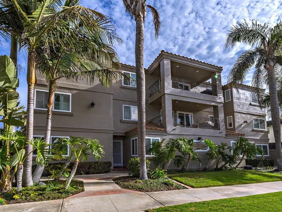 Front view of a multi-story residential building with balconies and palm trees in front.