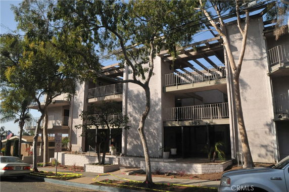Front view of a multi-story building with balconies and large trees in front.