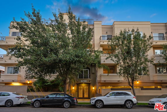 Front view of a multi-story residential building with balconies and trees in front.