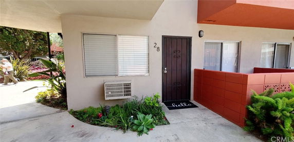 Front view of a residential building entrance with an air conditioning unit and potted plants.