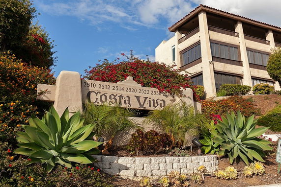 Front view of a multi-story building with large windows and a sign reading 'Costa Viva' in front.
