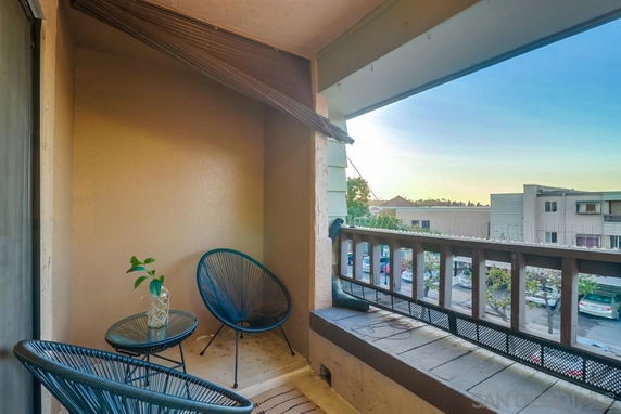 Balcony with two chairs and a table overlooking residential buildings and a parking area