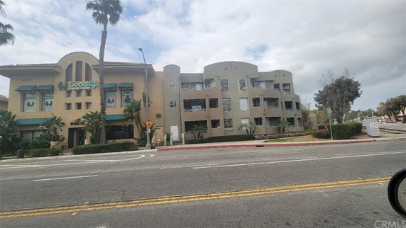 Front view of a multi-story building with balconies and palm trees in front.