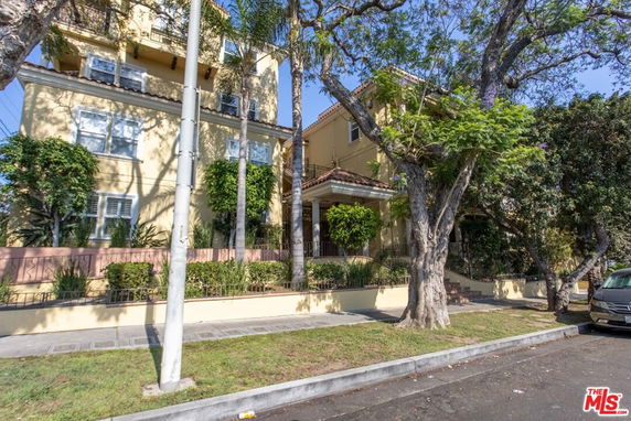 Front view of a multi-story residential building with trees and plants.