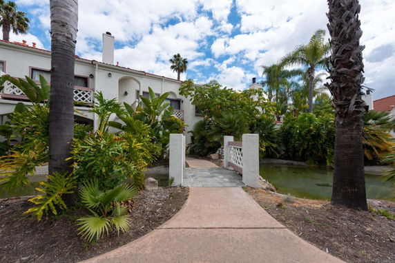 Front view of a multi-story house with a walkway and tropical plants.