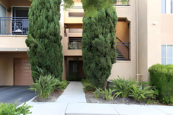 Front view of a multi-story apartment building with balconies and a pathway.