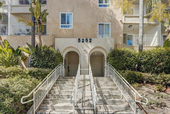 Front view of a building with stairs leading to an entrance and a balcony.