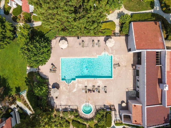 Aerial view of a large outdoor swimming pool with surrounding deck chairs and umbrellas, adjacent to a building with a red-tiled roof.