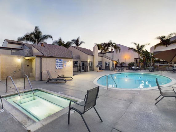 Outdoor swimming pool area with sun chairs and a hot tub, surrounded by buildings.