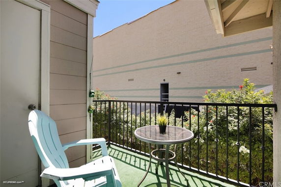 Small balcony area with a chair and table overlooking a wall and greenery.