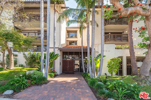 Front view of an apartment building with balconies and a brick walkway entrance.
